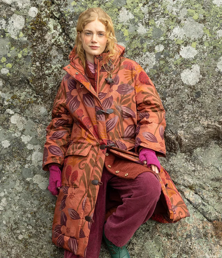 A woman wearing an orange winter jacket with a pattern from Gudrun Sjödén.