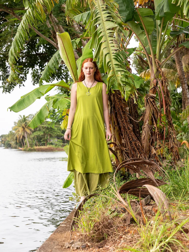 A woman standing by the water wearing a sleeveless green dress from Gudrun Sjödén.