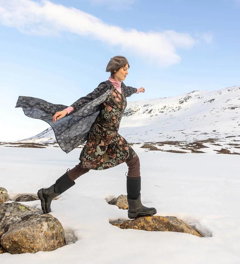 Gudrun Sjödénin vuoden 2025 joulumalliston vaatteisiin kerroksittain pukeutunut nainen, joka hyppää kahden kiven välillä.