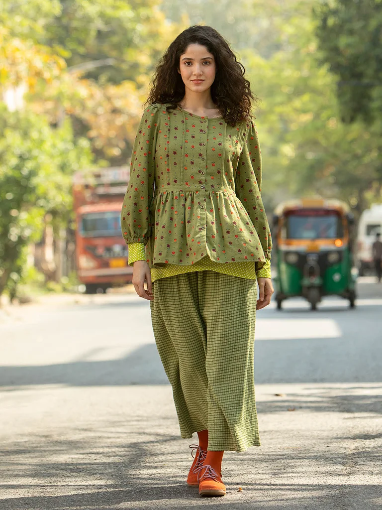 A woman wearing a patterned green blouse and a green skirt from Gudrun Sjödén.