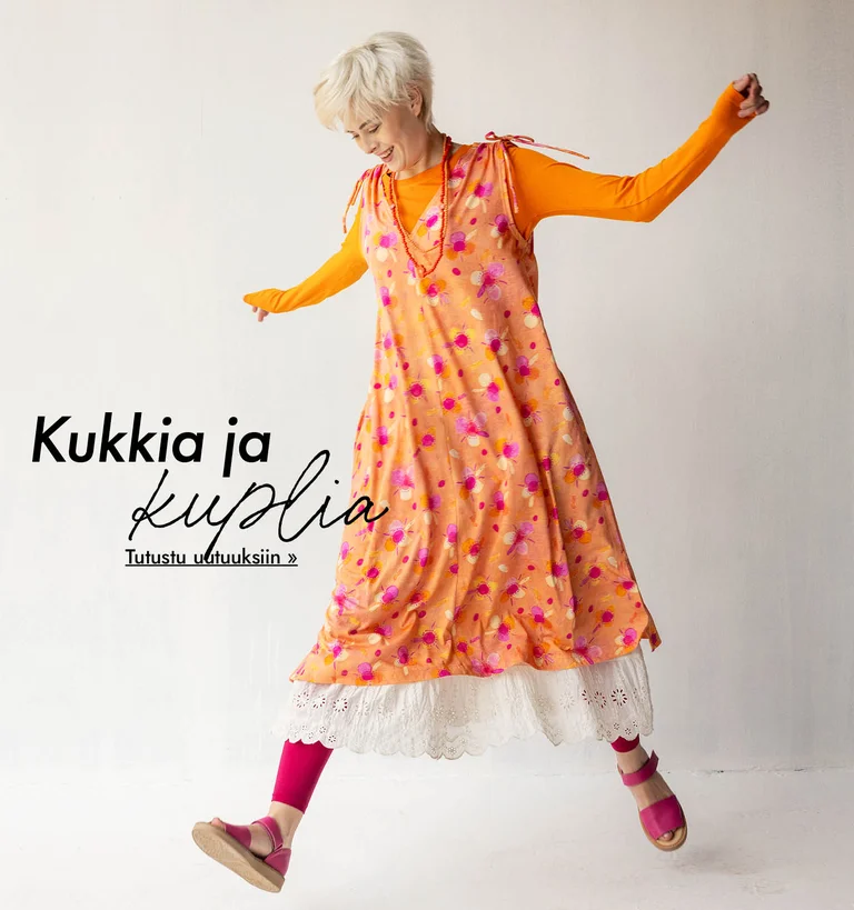 Kädet levällään kävelevä nainen, joka on pukeutunut Gudrun Sjödénin oranssiin kuviolliseen mekkoon, oranssiin puseroon ja valkoiseen alushameeseen.