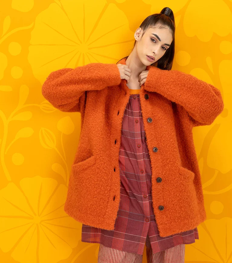 A woman wearing an orange bouclé jacket in wool from Gudrun Sjödén.