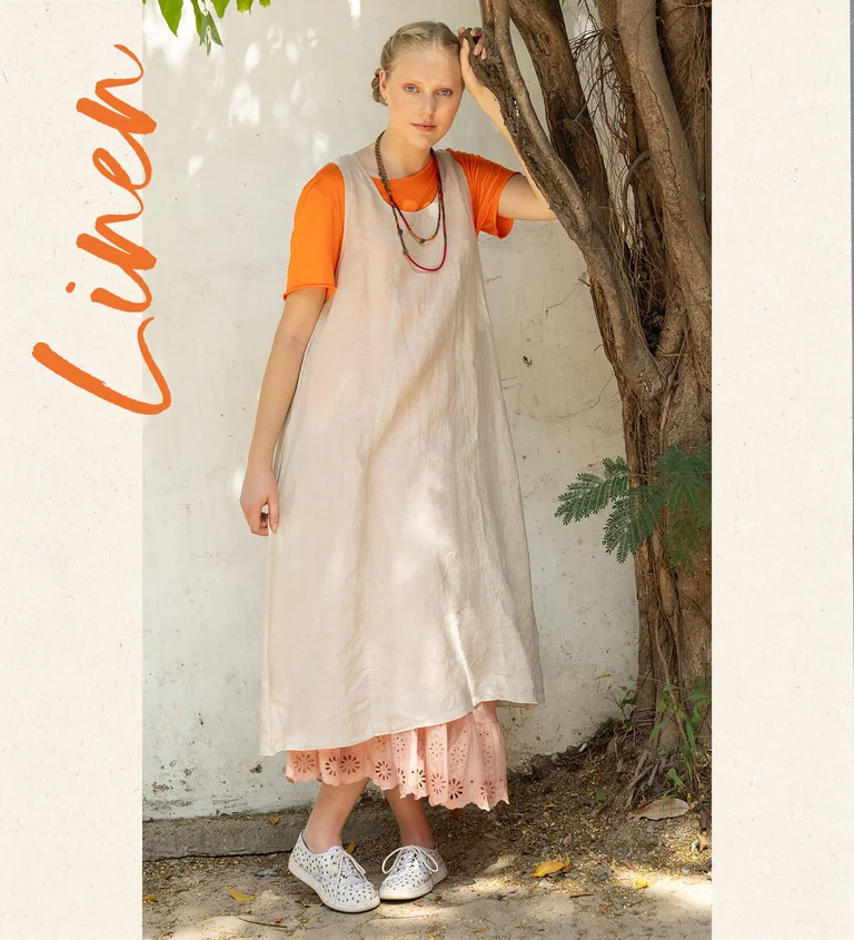 A woman wearing an orange top and natural-colored dress from Gudrun Sjödén.