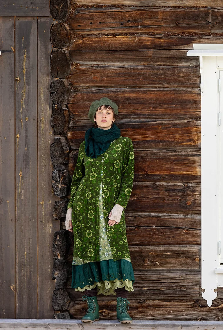A picture of three women standing next to a timber house wearing clothes from Gudrun Sjödén’s 2025 Christmas collection.