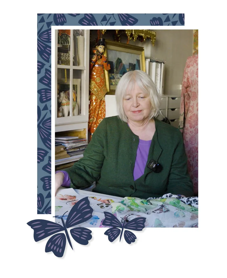 A woman standing on a beach, hands on her head, wearing a purple tunic from Gudrun Sjödén. With a purple frame and standout watercolour butterflies.