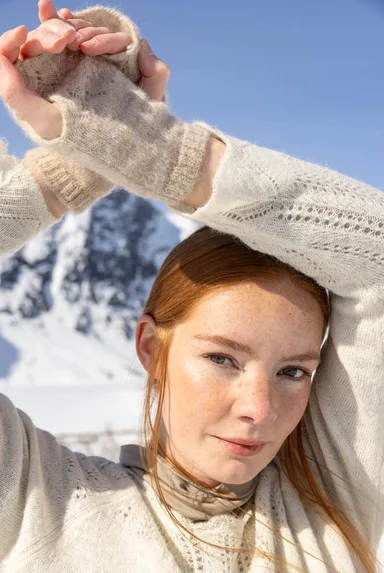 Lähikuva naisesta, joka on pukeutunut Gudrun Sjödénin vuoden 2025 joulumalliston valkoisiin neulevaatteisiin.