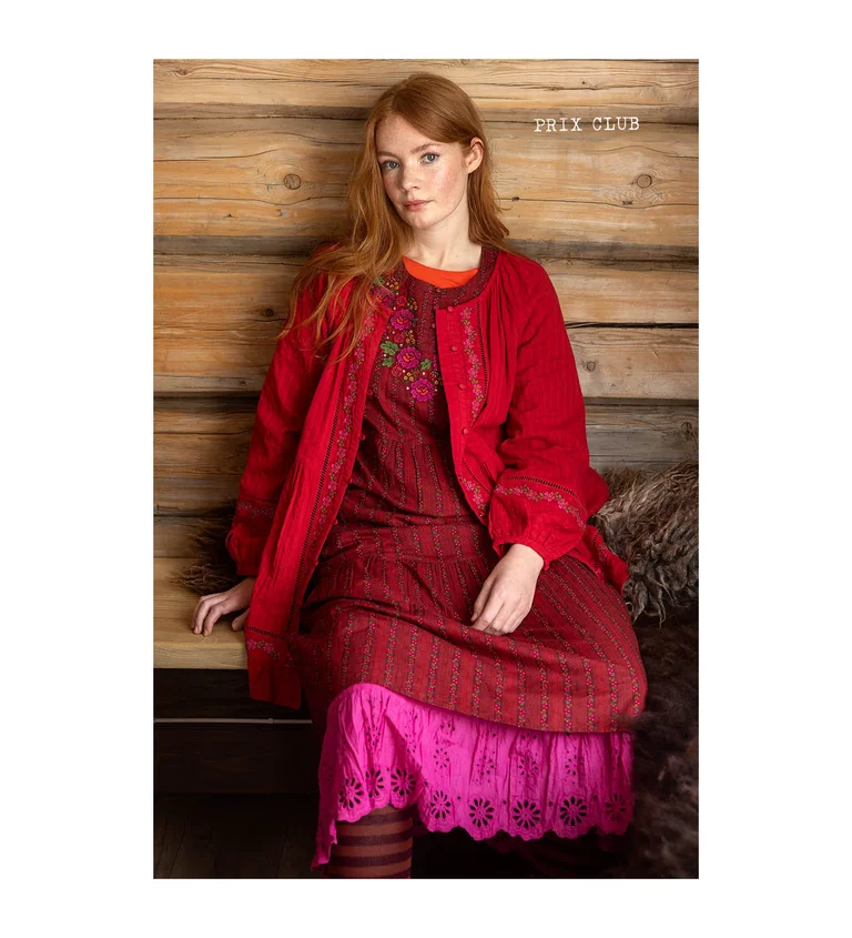 A woman sitting down wearing layers of pink and red clothes from Gudrun Sjödén’s 2025 Christmas collection.