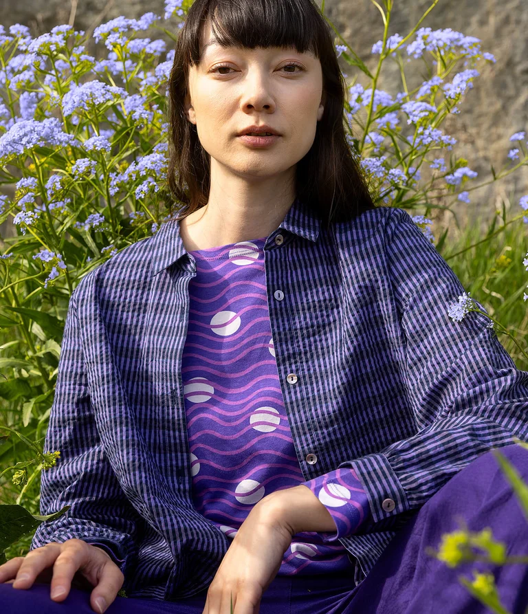 A woman wearing a purple jersey top and purple woven shirt from Gudrun Sjödén.