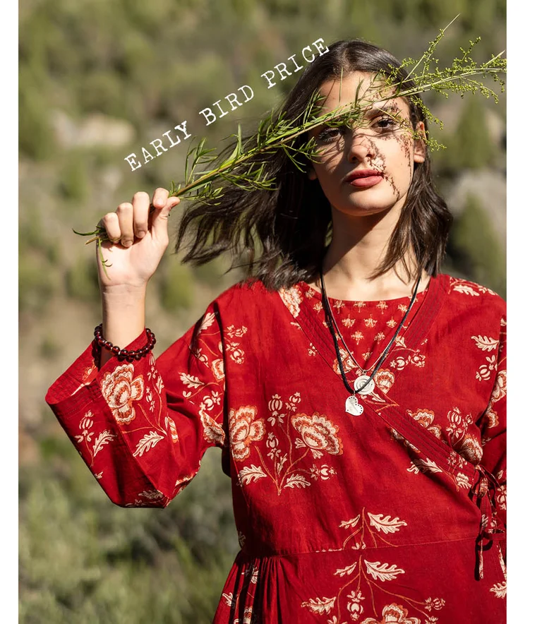 A woman holding a green branch in front of her face and wearing a red wrap dress from Gudrun Sjödén.