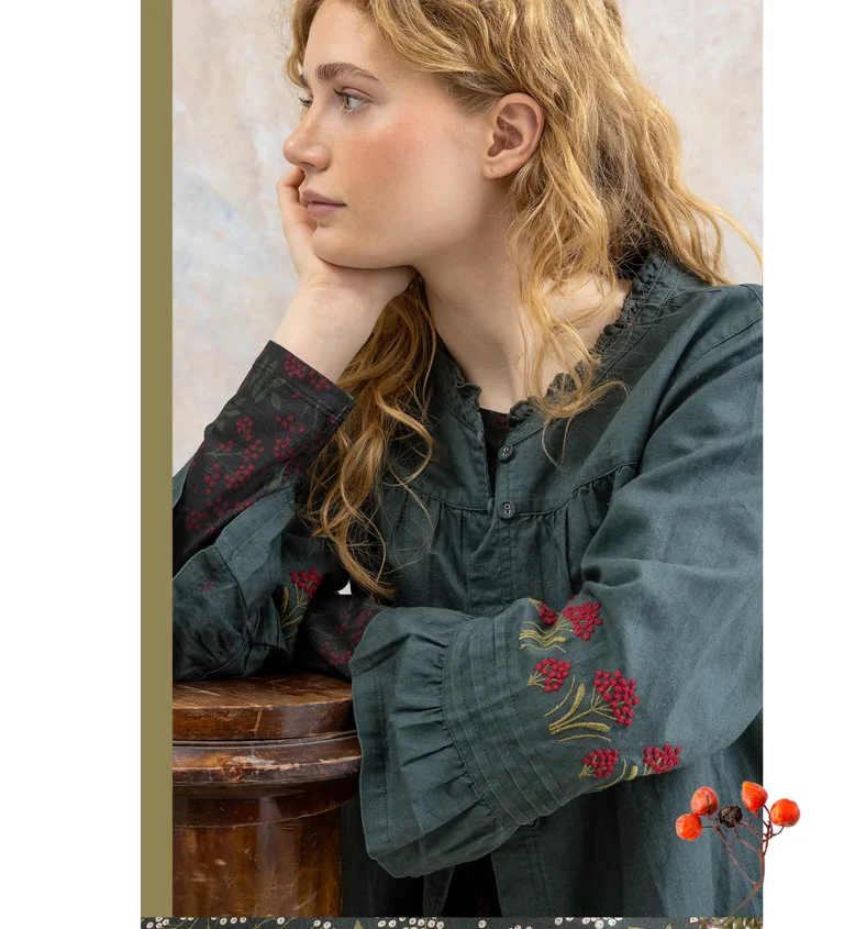 A woman wearing an embroidered blouse from Gudrun Sjödén.