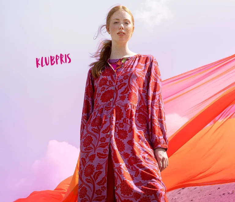 Et billede af en kvinde iført en mørk rosa cardigan over en rosa kjole fra Gudrun Sjödén.