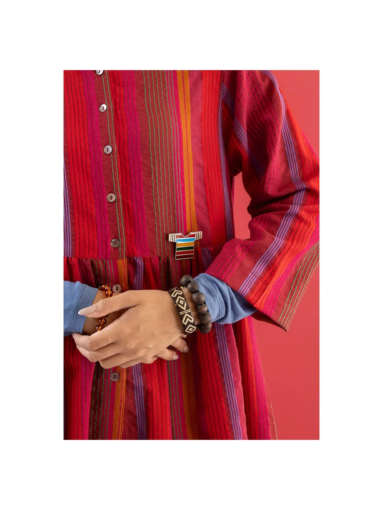 Un plan serré sur une femme portant une robe rayée et une broche en argent en forme de T-shirt provenant de la collection de Noël 2025 de Gudrun Sjödén