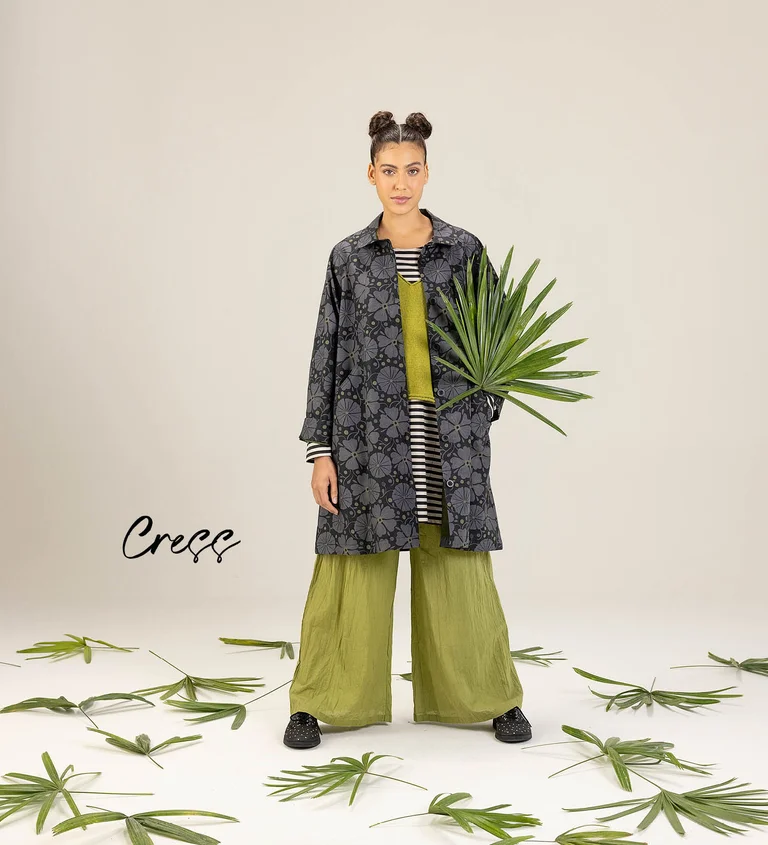 A woman wearing a patterned gray coat and green, wide-leg pants from Gudrun Sjödén.