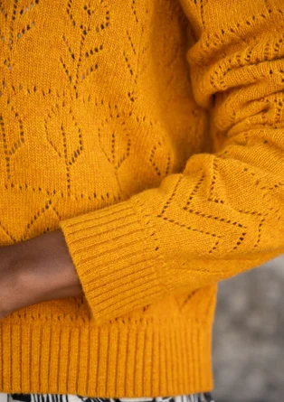 Detailansicht des Linken Ärmels einer Langarmstrickjacke mit Pointelle-Stricktechnik in der Farbe orange. 