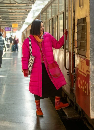 A woman boarding a train wearing a long pink down coat from Gudrun Sjödén.
