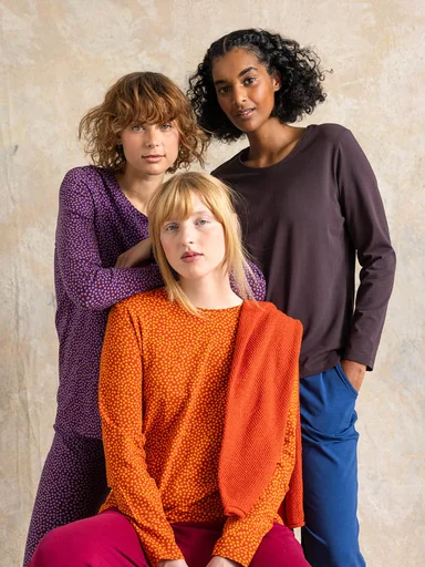 A woman wearing velour clothes, her arms full of velour clothes from Gudrun Sjödén.