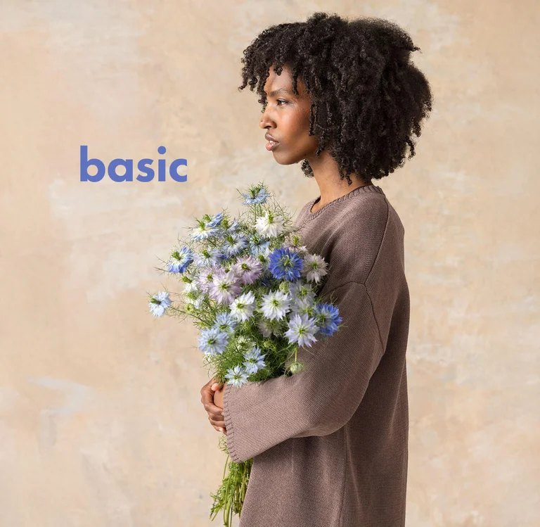 A woman, in profile, holding a bouquet and wearing a brown essentials top from Gudrun Sjödén.