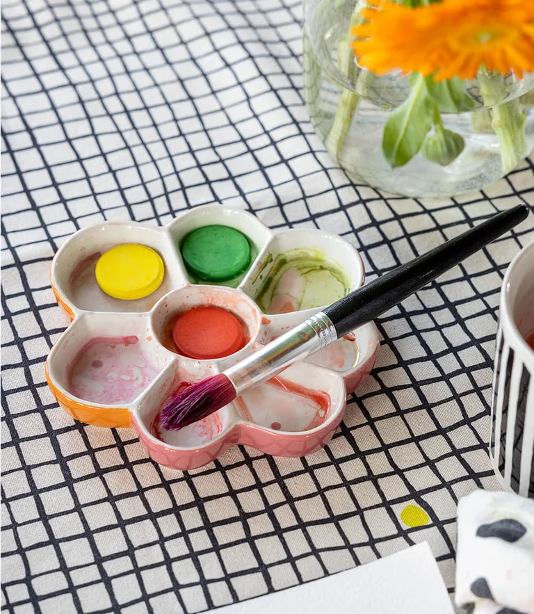 A paintbrush resting on a palette in the shape of a flower from Gudrun Sjödén.