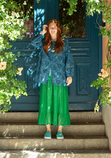 Femme portant une tunique bleue à fleurs et une jupe verte en tissu naturel