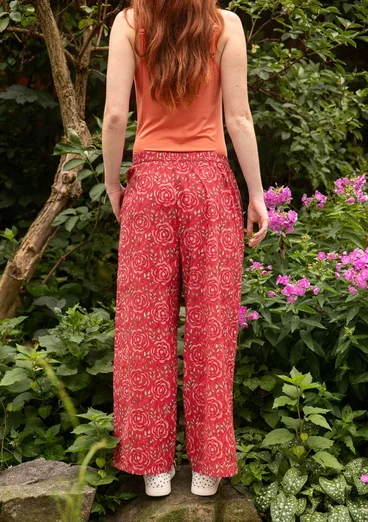 Rückansicht von roter Hose aus Naturmode mit rot-grünem Rosenmuster und orangefarbenen Top von Gudrun Sjödén.