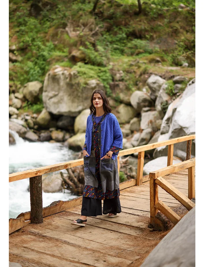 A woman walking over a wooden bridge wearing layers of clothes from Gudrun Sjödén.