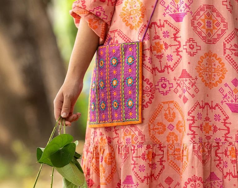 A woman holding a pink flower in her hand and wearing colorful clothing from Gudrun Sjödén.