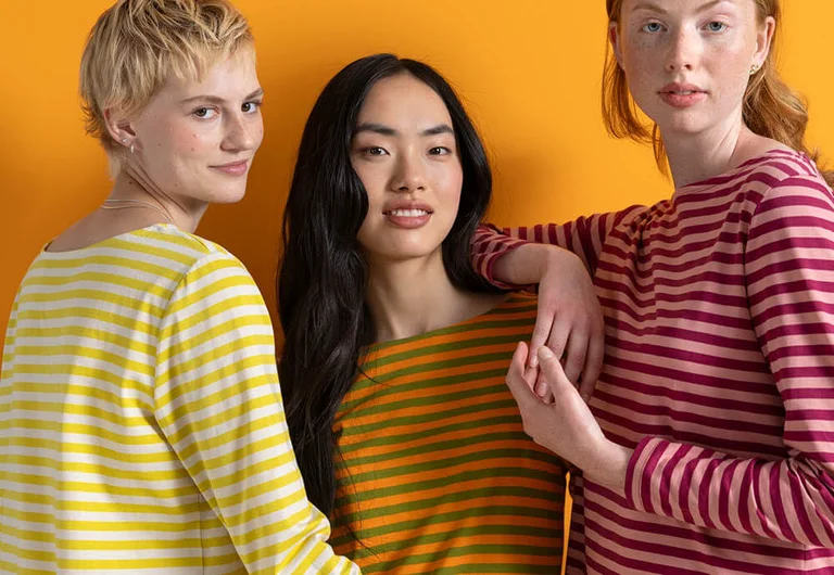 Three women standing next to each other wearing striped sweaters from Gudrun Sjödén.
