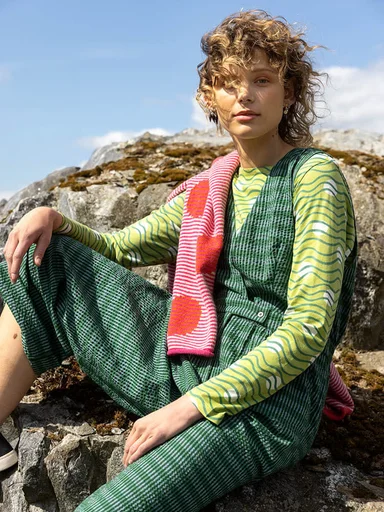 A woman sitting on a rock wearing layers of green clothes from Gudrun Sjödén.