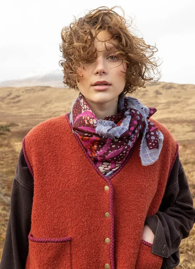A close-up of a woman wearing a red waistcoat and patterned scarf from Gudrun Sjödén.