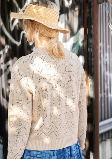 Vue arrière d'un cardigan à manches longues avec technique de tricotage pointelle dans la couleur sable clair. Combiné avec une robe tissée à motifs bleus.
