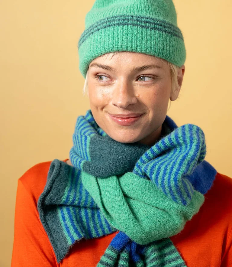 A woman wearing a knitted beanie and a knitted scarf in turquoise and blue from Gudrun Sjödén.