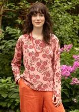 Rosa Langarm-Shirt mit roten Blumen. Das Model trägt dazu eine Hose in orange. 