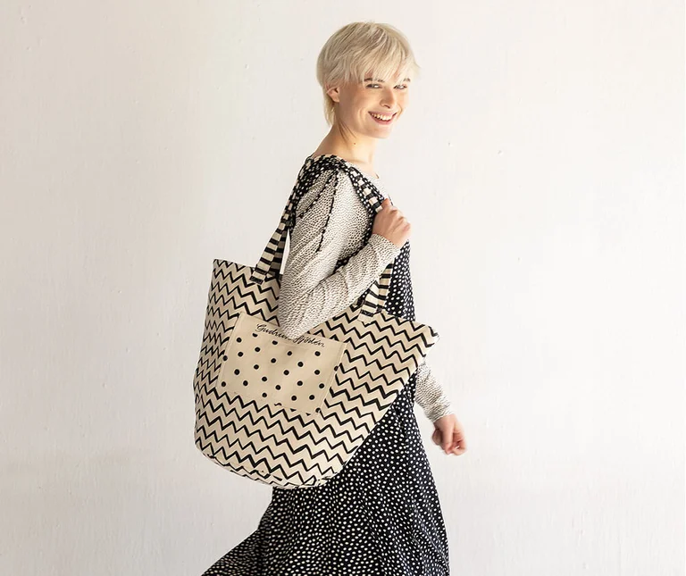 A woman carrying a black-and-white tote bag with a dotted and zigzag pattern from Gudrun Sjödén over her shoulder.