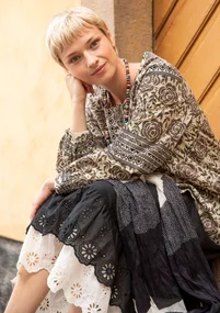 La femme porte des vêtements naturels de Gudrun Sjödén - une tunique en coton beige avec un motif de roses marron et un jupon noir et blanc.