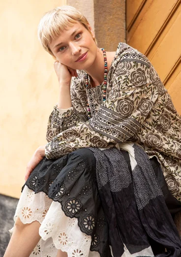 La femme porte des vêtements naturels de Gudrun Sjödén - une tunique en coton beige avec un motif de roses marron et un jupon noir et blanc.