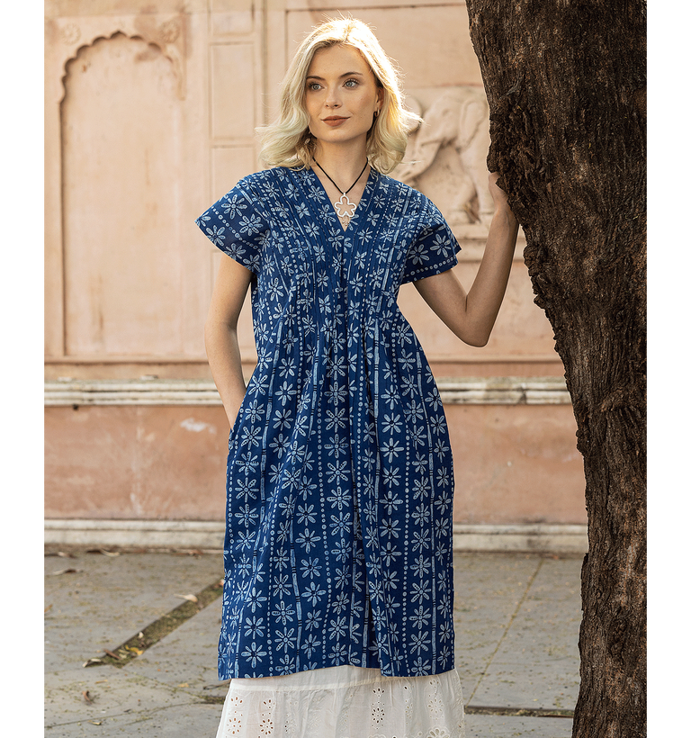 A woman leaning against a tree wearing a blue patterned dress from Gudrun Sjödén.