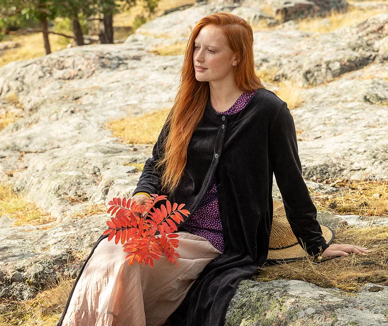A seated woman wearing a black velour dress from Gudrun Sjödén.