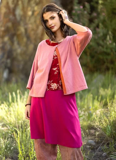 A woman standing outdoors wearing pink layered clothes from Gudrun Sjödén.