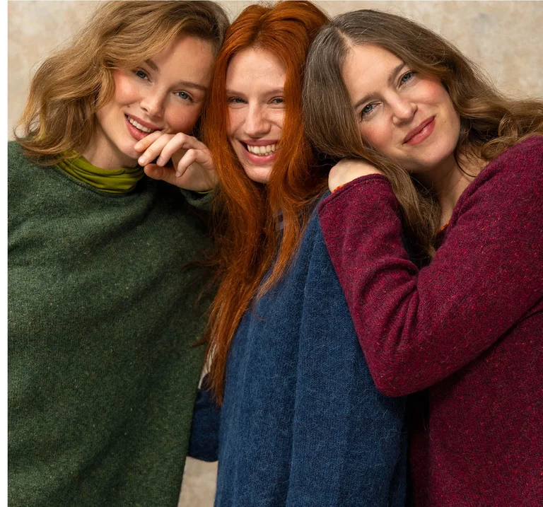 Three women close together wearing knitted sweaters in different colours from Gudrun Sjödén.