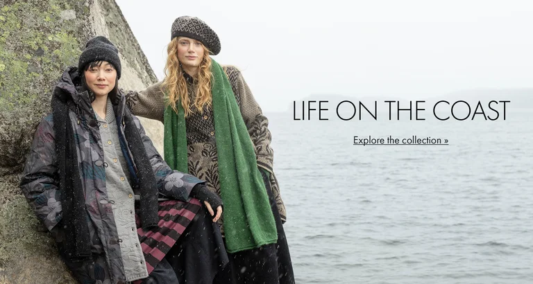 Two women posing by a rock face next to water, wearing clothes and accessories from Gudrun Sjödén’s 2025 Winter collection.