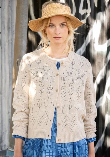 Cardigan à manches longues avec technique de tricotage pointelle dans la couleur sable clair. Combiné avec une robe tissée à motifs bleus.
