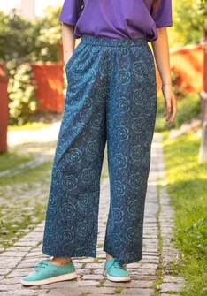 Frau trägt blaue Hose und lila T-Shirt von Gudrun Sjödén. Die Hose hat ein helllblaues Rosenmuster und ist aus Bio-Baumwollgewebe. 