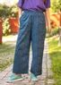 Une femme porte un pantalon bleu et un t-shirt violet de Gudrun Sjödén. Le pantalon a un motif de roses bleu clair et est en tissu de coton bio.