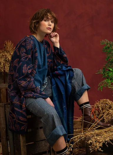 A seated woman wearing layers of clothes in low-key colours from Gudrun Sjödén.