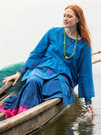 A woman holding a large, green leaf wearing layers of orange clothes from Gudrun Sjödén.