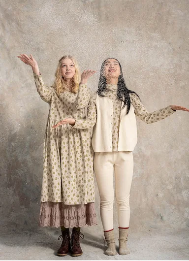 Two women with outstretched hands wearing layers of beige and white clothes from Gudrun Sjödén.