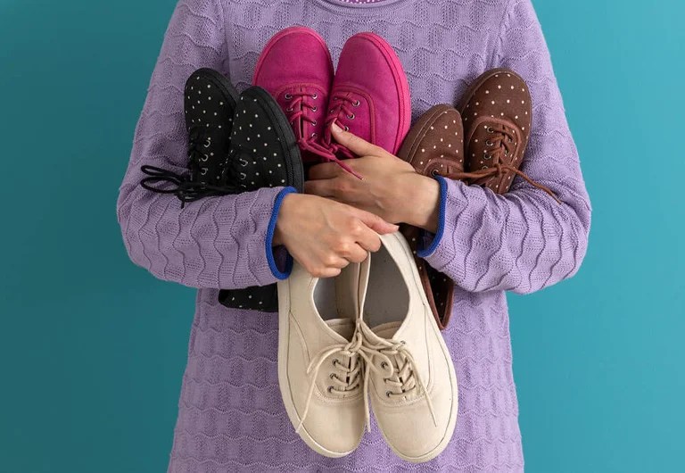 A woman with her arms full of different coloured shoes from Gudrun Sjödén.