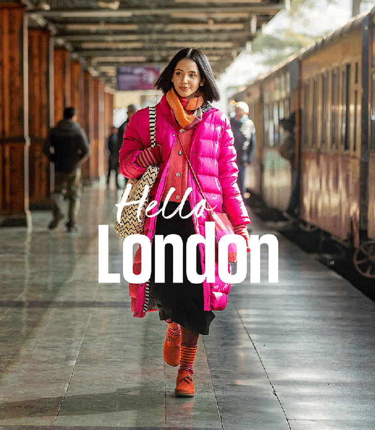 A woman walking along a train platform wearing layered clothes by Gudrun Sjödén.