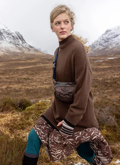 A woman walking in a windy mountain landscape wearing layers of clothes from Gudrun Sjödén.