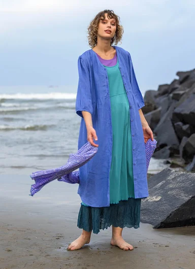 A woman standing on a beach wearing layers of clothes from Gudrun Sjödén.